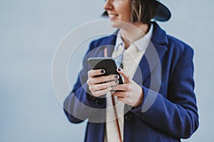 portrait outdoors of a young beautiful woman with stylish clothes posing with a modern hat and using mobile phone. lifestyle