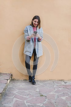 Portrait outdoors of a young beautiful woman with stylish clothes posing over yellow background and using mobile phone. lifestyle
