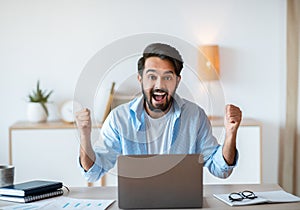 Portrait Of Overjoyed Eastern Man Celebrating Success With Laptop In Office