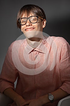 Portrait of overjoyed funny young Caucasian man wearing glasses, shirt in a strip siting indoors with happy face and
