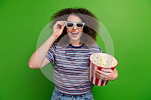 Portrait of overjoyed nice lady arm touch 3d glasses watch movie hold popcorn bucket isolated on green color background
