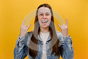 Portrait of overjoyed young woman showing rock and roll hand sign, screaming and gesturing to heavy metal, rock music, wearing