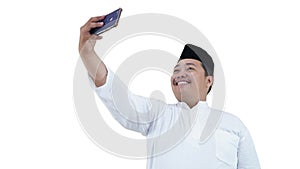 Portrait of overweight muslim man with head cap or songkok taking selfie with his smartphone photo