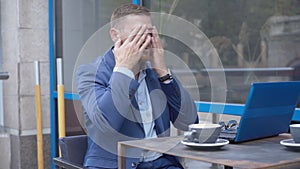 Portrait of overworked Caucasian businessman surfing Internet on laptop. Tired handsome man taking off eyeglasses