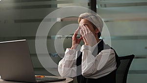 Portrait of overworked mature adult woman suffering from eye strain while working on laptop on evening, sitting at