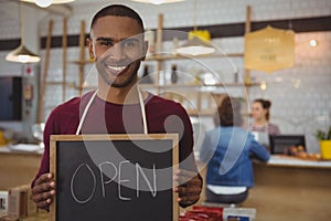 Portrait of owner with open sign in cafe