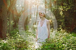 Portrait of pacified middle-aged woman standing in forest among plants, trees on sunny day, enjoying weather, posing. photo