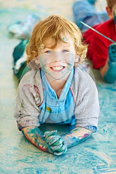 Portrait, paint and a boy lying on the floor of a studio for creative expression or education at school. Art, painting