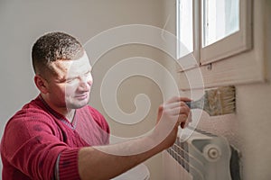 Portrait of painter young man in red t-shirt painting the wall in white color, with paint roller brush, home decor