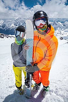 Portrait of a pair of young skiers athletes man and woman in ski masks with skis stand and look at the camera on the