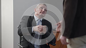 Portrait of paralyzed grey-haired senior man shaking hands with unrecognizable business partner. Paraplegic Caucasian