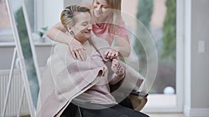 Portrait of paralyzed woman sitting in wheelchair as empathic friend covering woman with blanket. Supported Caucasian