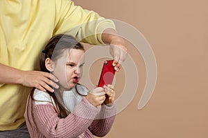 Portrait of parent taking smartphone away from girls hands, beige background. Angry daughter hold tight phone and resist