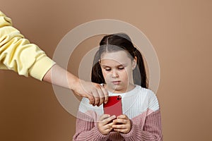 Portrait of parent taking smartphone away from girls hands, beige background. Little daughter hold tight phone and