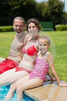 Portrait of parents and daughter sitting on poolside in pool water