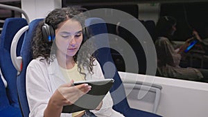 portrait of passenger woman in train, lady listening to music and viewing video in tablet