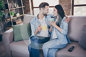 Portrait of passionate caring married couple sit couch man woman hug embrace drink beverage mug enjoy together free time