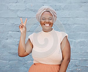 Portrait, peace and hand gesture with a business black woman on a blue brick wall with a smile. Hand, emoji and