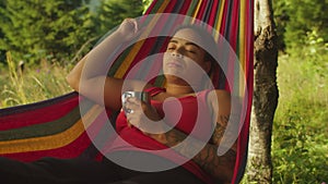 Portrait of peaceful lovely african american woman traveler resting in hammock in summer nature