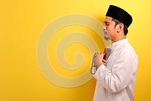 Portrait of peaceful Young Asian Muslim man holding Quran and prayer beads with a copy space aside