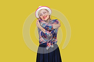 Portrait of peacful happy modern stylish mature woman in casual style with hat, eyeglasses standing, hugging herself with closed photo