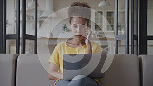 Portrait of a pensive African American woman working on laptop computer indoors in her apartment
