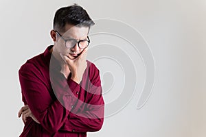 Portrait of pensive asian man in glasses looking up at copy space, touching his chin on grey background. Adult thinking and making