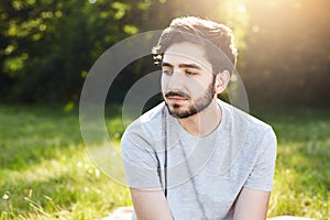 Portrait of pensive bearded male with stylish hairdo looking down with his charming big dark eyes thinking over his life enjoying