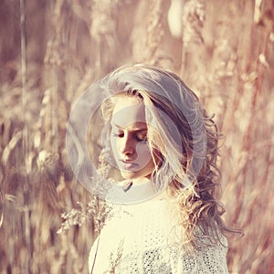 Portrait of pensive beautiful blonde girl in a field in white pullover, the concept of health and beauty