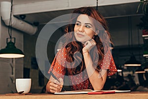 portrait of pensive blogger sitting at table with notebook