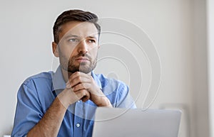 Portrait Of Pensive Businessman Sitting At Workplace With Laptop And Looking Away