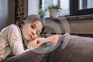 portrait of pensive child looking at camera while sitting on sofa