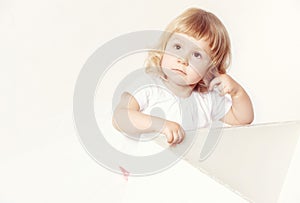 Portrait of a pensive cute little girl in a white dress on white background.