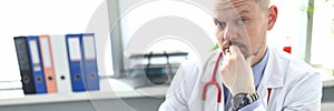 Portrait of pensive doctor at workplace with laptop in clinic