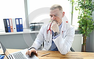 Portrait of pensive doctor at workplace with laptop in clinic