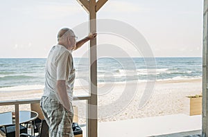 Portrait of a pensive elderly man standing on the terrace of a cafe and looking at the sea