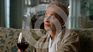 Portrait pensive elderly woman enjoying red wine glass at home. Old aged lady