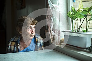 Portrait of pensive elderly woman sadly looking out the window.