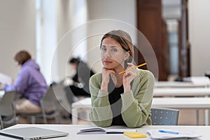 Portrait of pensive focused middle-aged woman mature female student in library interior