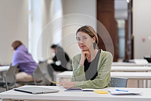 Portrait of pensive focused middle-aged woman mature female student in library interior