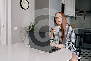 Portrait of pensive freelancer female remote working or studying on laptop computer sitting at table, holding in hand