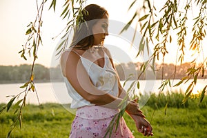 Portrait of a pensive girl on the bank of the river, in the willow foliage