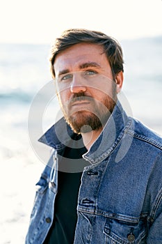 Portrait of a pensive man in a denim jacket against the background of the sea. Close-up