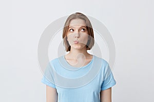 Portrait of pensive pretty young woman in blue t shirt thinking and feels puzzled isolated over white background Looks to the side