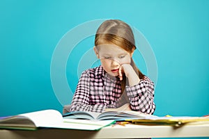 Portrait pensive pupil sitting at table with lot of books and fascinating reading on isolated blue. Schoolgirl does