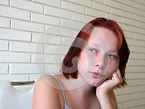 Portrait of a pensive red-haired teenage girl against a brick wall