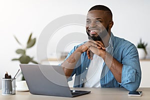 Portrait of pensive smiling black freelancer sitting at desk in home office