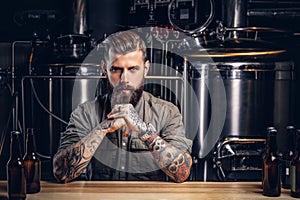 Portrait of a pensive tattooed hipster male with stylish beard and hair in the shirt in indie brewery.