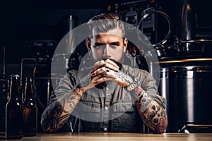 Portrait of a pensive tattooed hipster male with stylish beard and hair in the shirt in indie brewery.