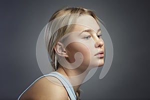 Portrait of a pensive teenage girl. Cute blonde girl in a T-shirt on a dark gray background. Problems during difficult puberty.